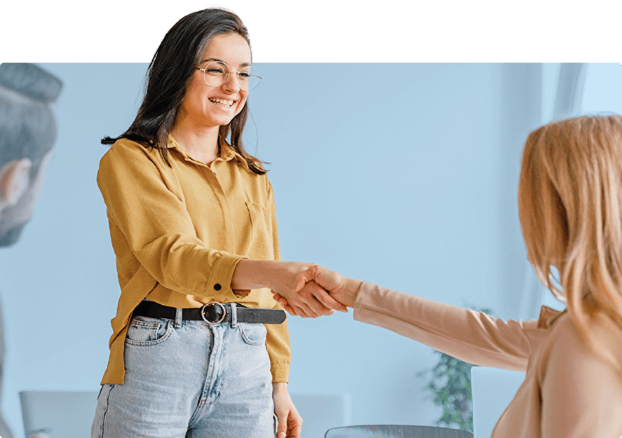 Zwei Geschäftsfrauen schütteln sich die Hände bei einem Geschäftstreffen. Beide lächeln, was auf eine erfolgreiche Verhandlung im B2B-Bereich hinweist.