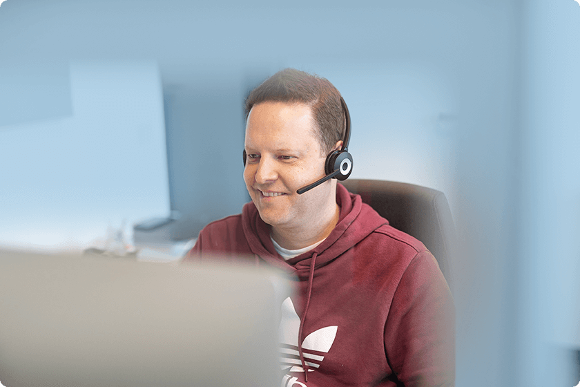 in lächelnder Kundenservice-Mitarbeiter mit Headset arbeitet an einem Computer