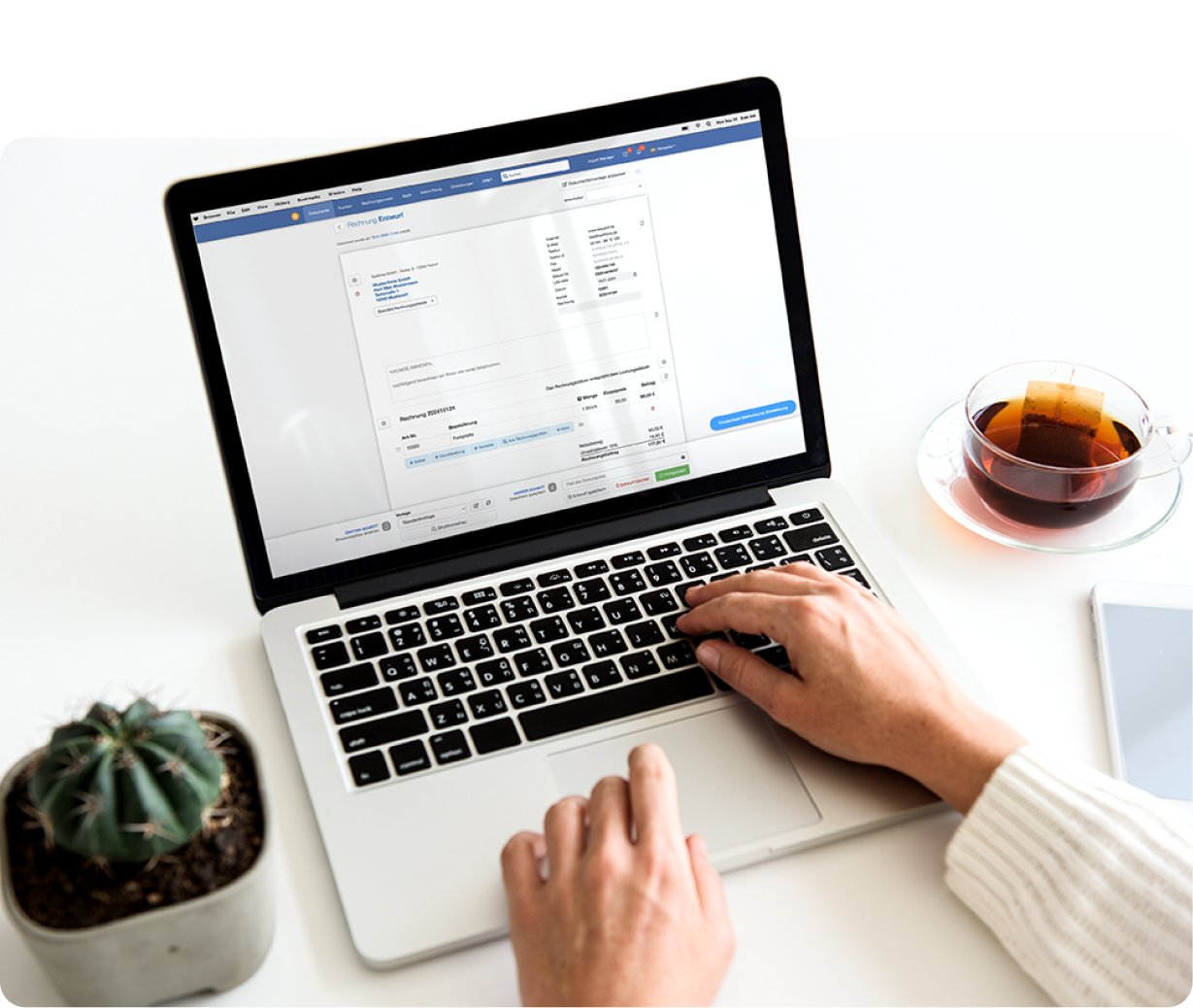Person erstellt eine E-Rechnung auf einem Laptop mit einer Tasse Tee und einer Pflanze im Hintergrund