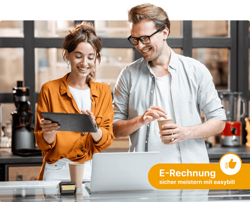 Zwei lächelnde Personen, eine Frau und ein Mann, arbeiten gemeinsam an einem Tablet und einem Laptop in einem modernen Büro. Ein gelbes Icon mit einem Daumen hoch und der Text “E-Rechnung sicher meistern mit easybill” ist in der unteren rechten Ecke des Bildes platziert.