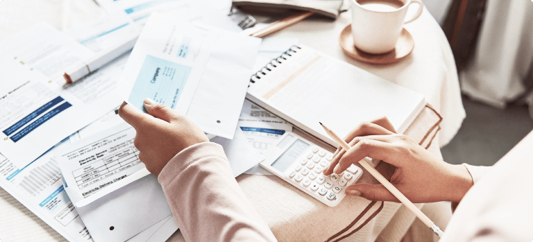 Person bei der Buchhaltung, die mit einem Taschenrechner und Rechnungen arbeitet, um die Mehrwertsteuer zu berechnen.